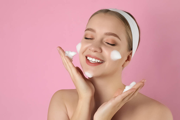 Young woman washing face with cleansing foam on pink background. - Foto, Bild
