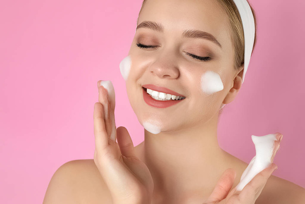 Young woman washing face with cleansing foam on pink background. - Foto, Imagem