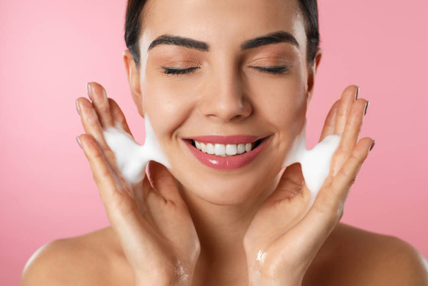 Young woman applying cosmetic product on pink background, closeup. Washing routine - Photo, image