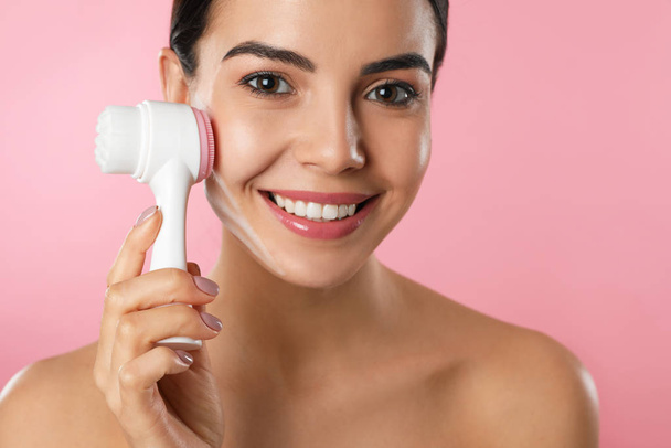 Young woman using facial cleansing brush on pink background, closeup. Washing accessory - Photo, Image