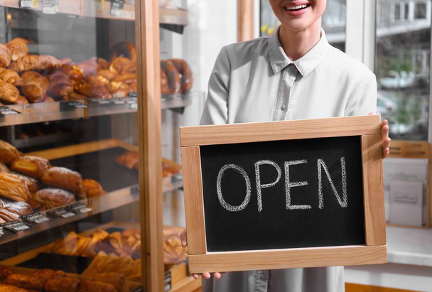 Female business owner holding OPEN sign in bakery, closeup - Foto, imagen
