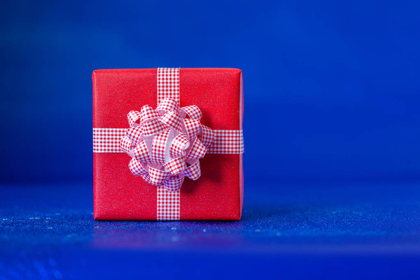 Red gift box with big bow on blue background. Festive concept. - Фото, зображення