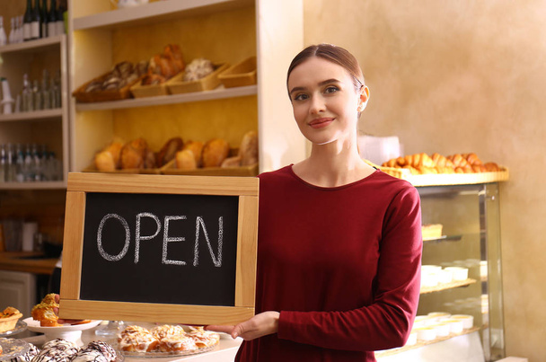 Female business owner holding OPEN sign in bakery - Valokuva, kuva