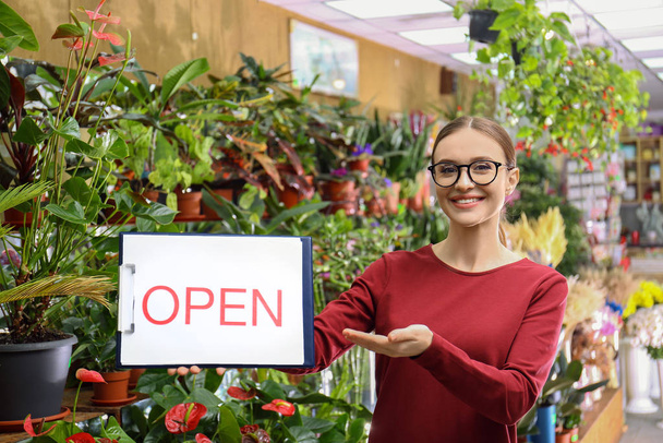 Female business owner holding OPEN sign in flower shop - Foto, afbeelding