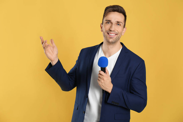 Young male journalist with microphone on yellow background - 写真・画像