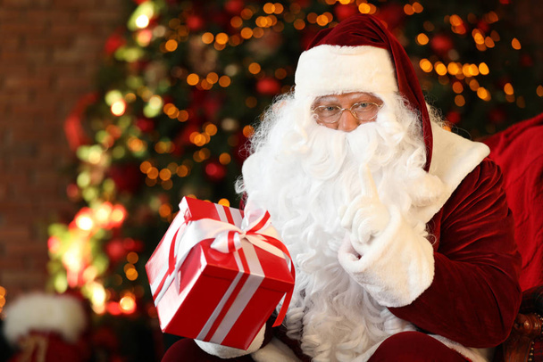 Santa Claus with gift box near Christmas tree indoors - Фото, зображення