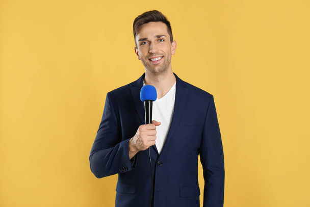 Young male journalist with microphone on yellow background - Fotó, kép