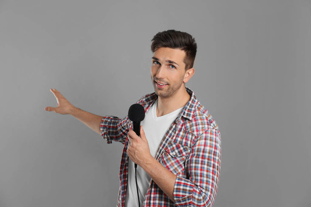 Young male journalist with microphone on grey background - Photo, Image