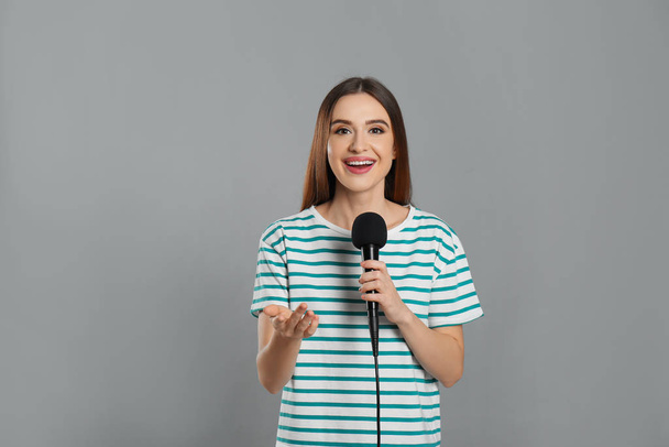Young female journalist with microphone on grey background - Foto, Bild