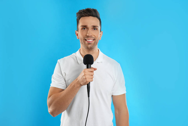 Joven periodista masculino con micrófono sobre fondo azul
 - Foto, imagen