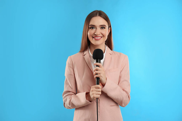 Young female journalist with microphone on blue background - Φωτογραφία, εικόνα