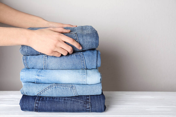 Woman folding stylish jeans on white wooden table, closeup. Space for text - Fotoğraf, Görsel