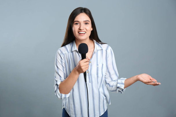 Young female journalist with microphone on grey background - Fotoğraf, Görsel