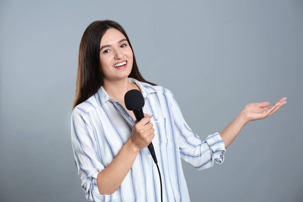 Young female journalist with microphone on grey background - Foto, afbeelding