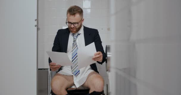 Man with documents in toilet looking puzzled - Materiał filmowy, wideo