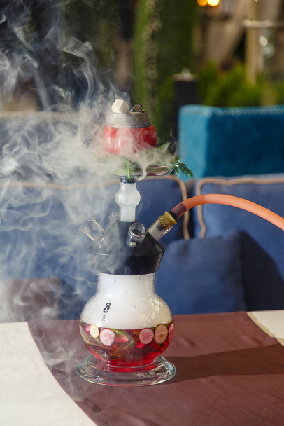 Hookah on vegetables. Hookah with a round transparent flask, which contains chopped vegetables: pepper, cucumber, radishes, herbs. Vegetables are filled with red liquor. Lots of smoke. - Фото, зображення