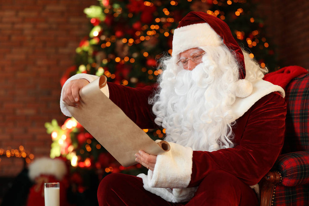 Santa Claus with wish list near Christmas tree indoors - Foto, Imagen