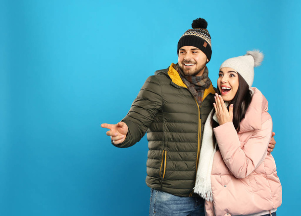 Happy young couple in warm clothes on blue background, space for text. Winter vacation - Foto, afbeelding