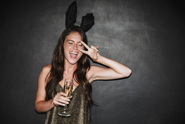 Imagen de una mujer sosteniendo una copa de champán mientras hace gestos de señal de paz
 - Foto, imagen