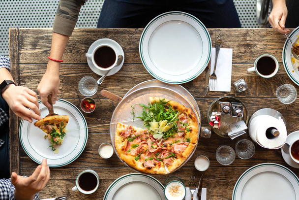 Friends at the table eat pizza. The company gathered in a restaurant. Lunch, a snack at work. Pizza party. People take slices of pizza. Table setting. People eat fast food. Coffee on the table. - Valokuva, kuva