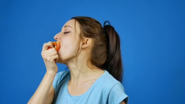 Mujer sonriente con dientes sanos comiendo manzana roja sobre fondo azul en el estudio. Concepto de dieta. Comida vegetariana
. - Metraje, vídeo
