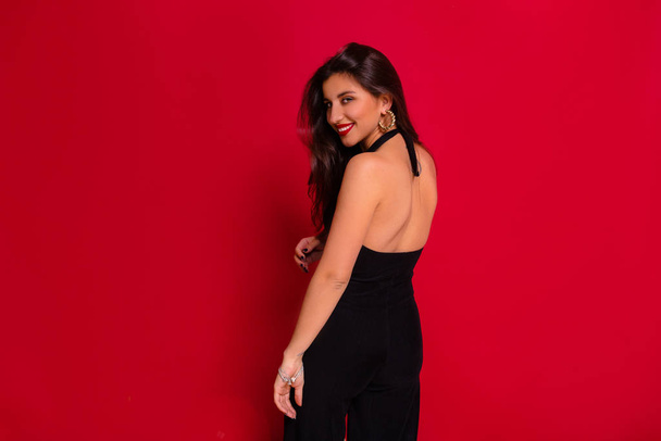 Studio portrait of elegant charming woman wearing black dress with bare back posing at camera over red background  - Foto, Bild