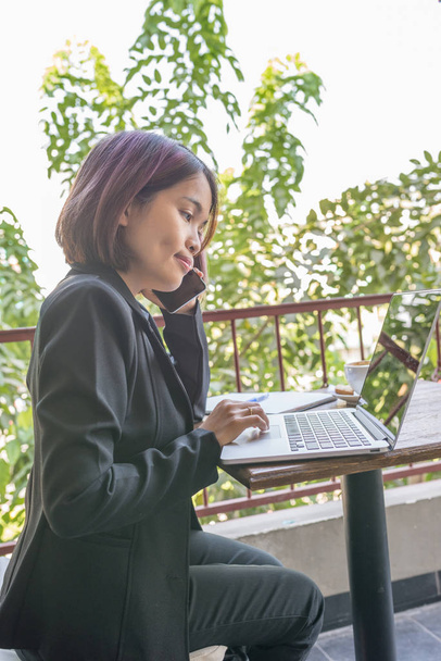 Woman wearing black suit working on laptop and using cellphone - Foto, Imagem