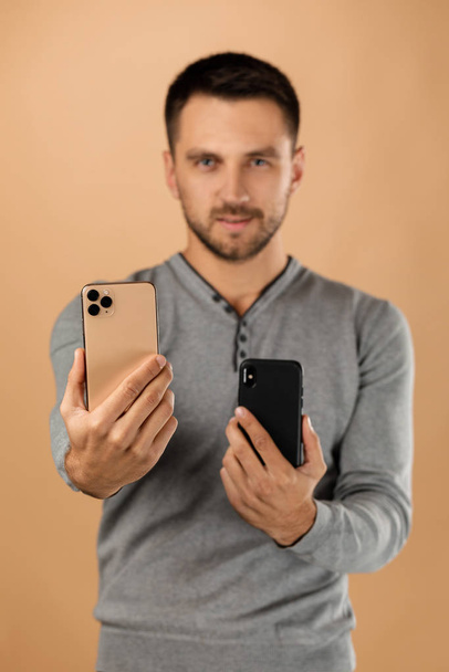 handsome young man compares two phones - Φωτογραφία, εικόνα