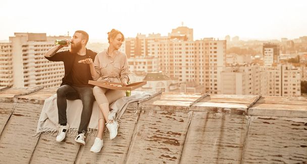 Young couple enjoying pizza and beer on rooftop - Фото, зображення