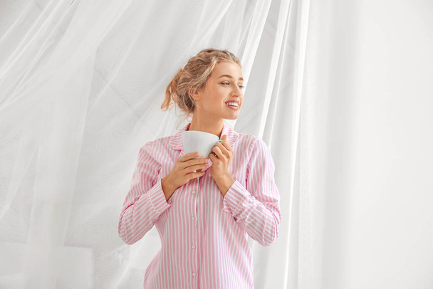 Aamulla kaunis nuori nainen kupin kahvia lähellä ikkunaa
 - Valokuva, kuva