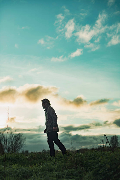 Μυστηριώδης άνθρωπος στο αγροτικό τοπίο με συννεφιασμένο ουρανό στο ηλιοβασίλεμα. - Φωτογραφία, εικόνα