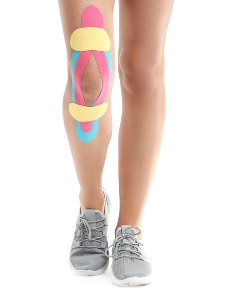 Αθλητική γυναίκα με ταινία physio εφαρμόζεται στο γόνατο σε λευκό φόντο - Φωτογραφία, εικόνα