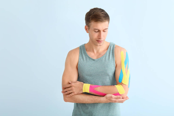 Sporty man with physio tape applied on arm against light background - Foto, Imagem