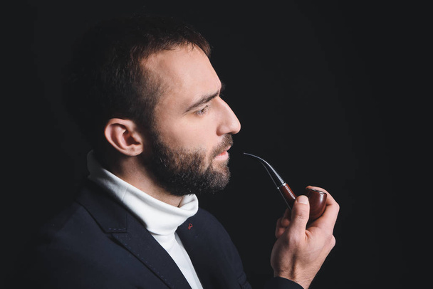 Portrait of stylish young man with smoking pipe on dark background - Photo, Image