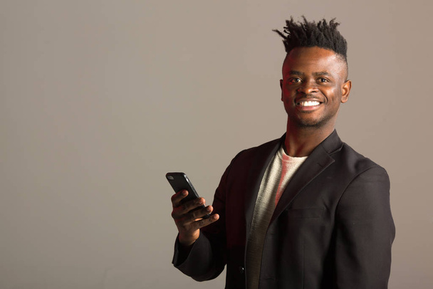handsome african man in a black suit on a gray background with a phone in his hand - Fotografie, Obrázek