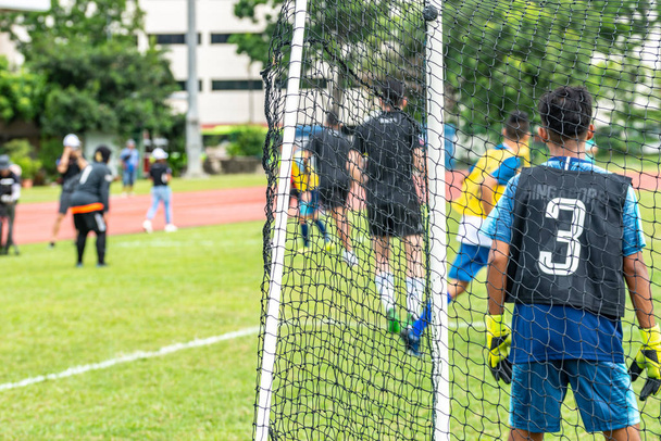 Selective focus. Blurred bokeh background. Back view of soccer goal post and Asian male goalkeeper and other players. - Photo, Image