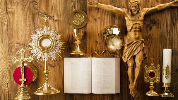 Tema Iglesia Católica Romana. La Cruz, la Santa Biblia, la monstrancia, el rosario y el cáliz dorado sobre una mesa rústica de madera
 - Foto, Imagen