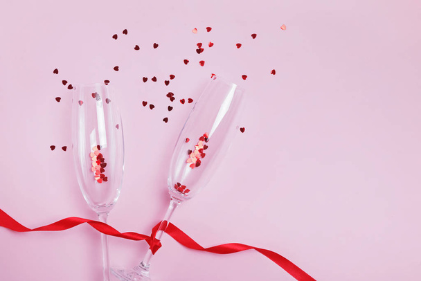 Two champagne glasses, red ribbon and heart shaped confetti splashes. - Photo, Image