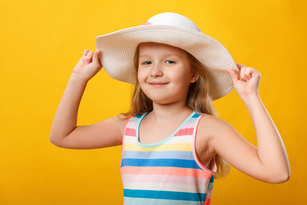 Summer portrait of a cute little girl. A child in a dress and hat on a yellow background - Фото, изображение