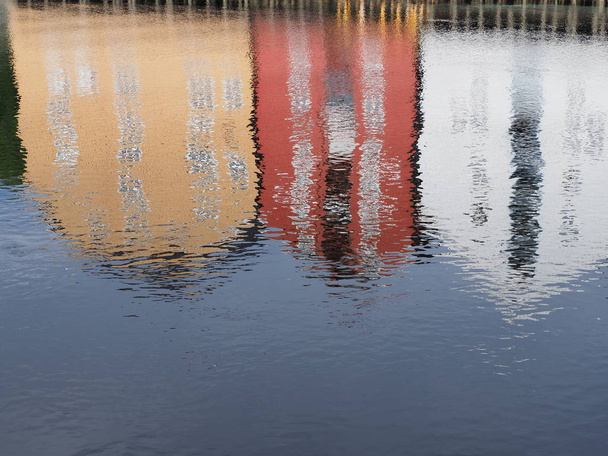 Water reflection of three colorful wooden houses at Nidelva river in european Trondheim city, Norway in 2019 warm sunny summer day in the morning on July. - Foto, Imagen