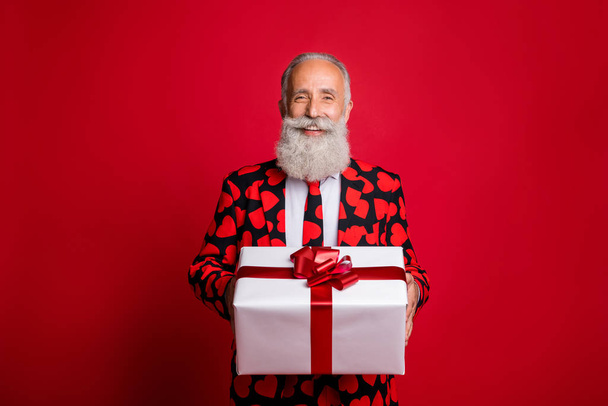Photo of funky mature guy amour cupid character role showing big gift box holiday courier wear stylish hearts pattern suit costume shirt tie isolated red color background - Φωτογραφία, εικόνα