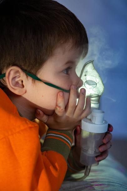 Chłopiec w masce, leczy drogi oddechowe nebulizatorem. Dziecko siedzi z nebulizatorem w ustach, inhalator, leczenie zapalenia oskrzeli - Zdjęcie, obraz