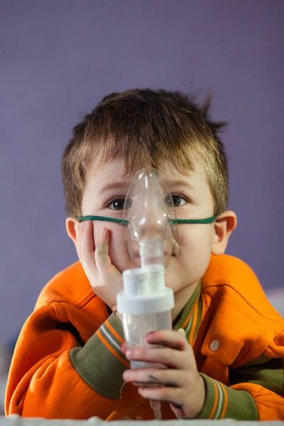 Niño enmascarado, trata las vías respiratorias con un nebulizador en casa. El bebé se sienta con un nebulizador en la boca, inhalador, tratamiento de la bronquitis
 - Foto, imagen