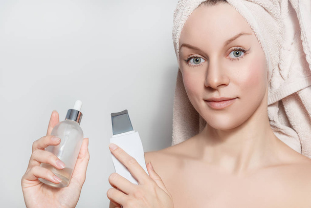 Young beautiful woman holding beauty device and serum bottle.  Female facial skin care concept - Foto, imagen