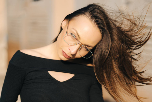 Aantrekkelijke jonge brunette vrouw het dragen van een zwart top en transparante bril poseren op straat - Foto, afbeelding