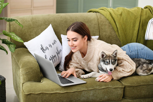 Evde dinlenen komik köpekli ve laptoplu genç bir kadın. - Fotoğraf, Görsel