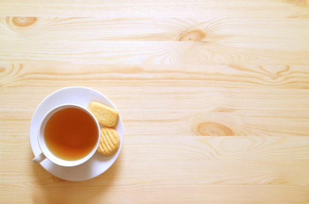 Bovenaanzicht van een kopje warme thee en koekjes op natuurlijke houten tafel met vrije ruimte voor tekst en design - Foto, afbeelding