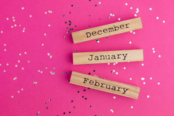 Wooden calendar winter months December January February. Pink background with multicolored confetti. Flat lay style. Top view - Photo, Image