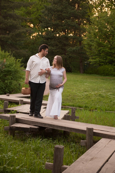 A man with a pregnant woman on the bridge in the park - Fotoğraf, Görsel