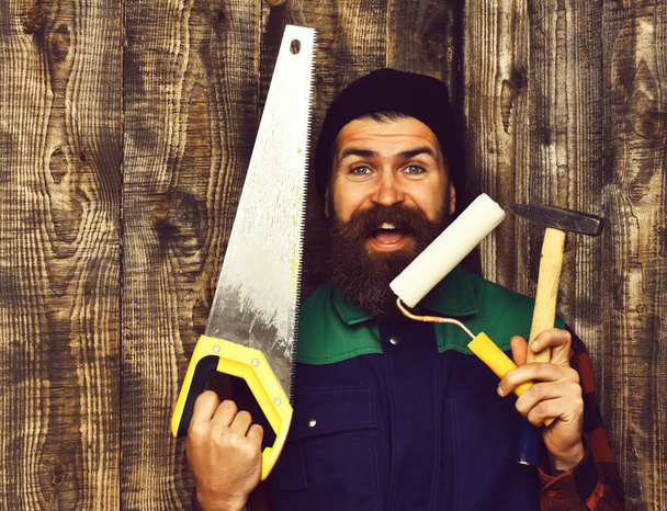 bearded builder holding various building tools with happy face - Foto, afbeelding